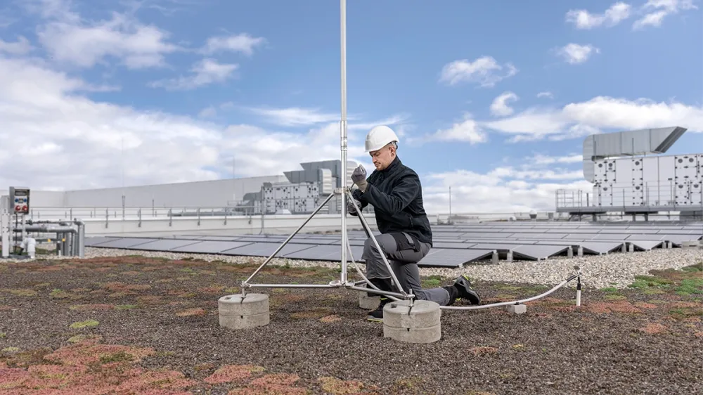Man wearing a safety helmet installs a lightning rod on a green roof with a solar power system.