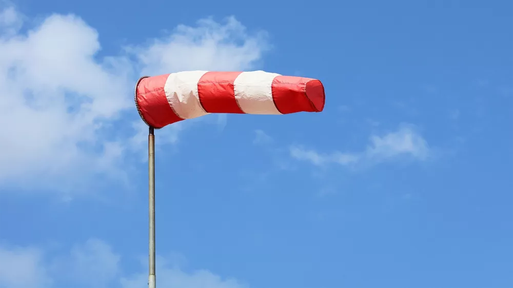 Red and white windsock on a pole against a blue sky with clouds.