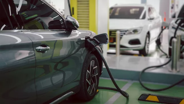 Electric car charging at indoor EV charging station, plug connected to vehicle with another electric car in background.
