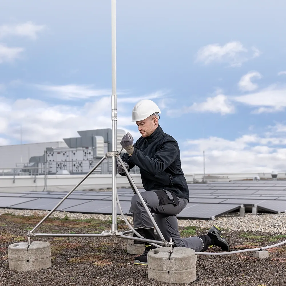 Une personne portant un casque blanc et des vêtements sombres, agenouillée sur le sol et travaillant sur une construction composée d’une tige de capture et de poids en béton.