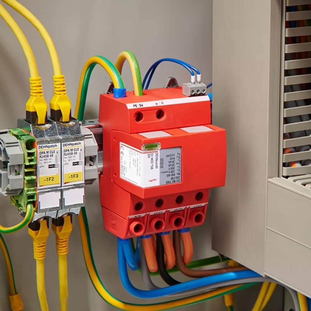 Parafoudre rouge, monté et câblé à côté d’une armoire électrique ouverte.