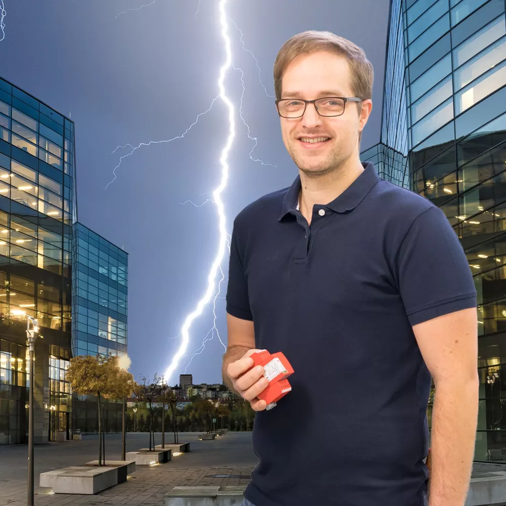 Man holding a red surge protection device, standing between modern office buildings with a lightning strike in the background.