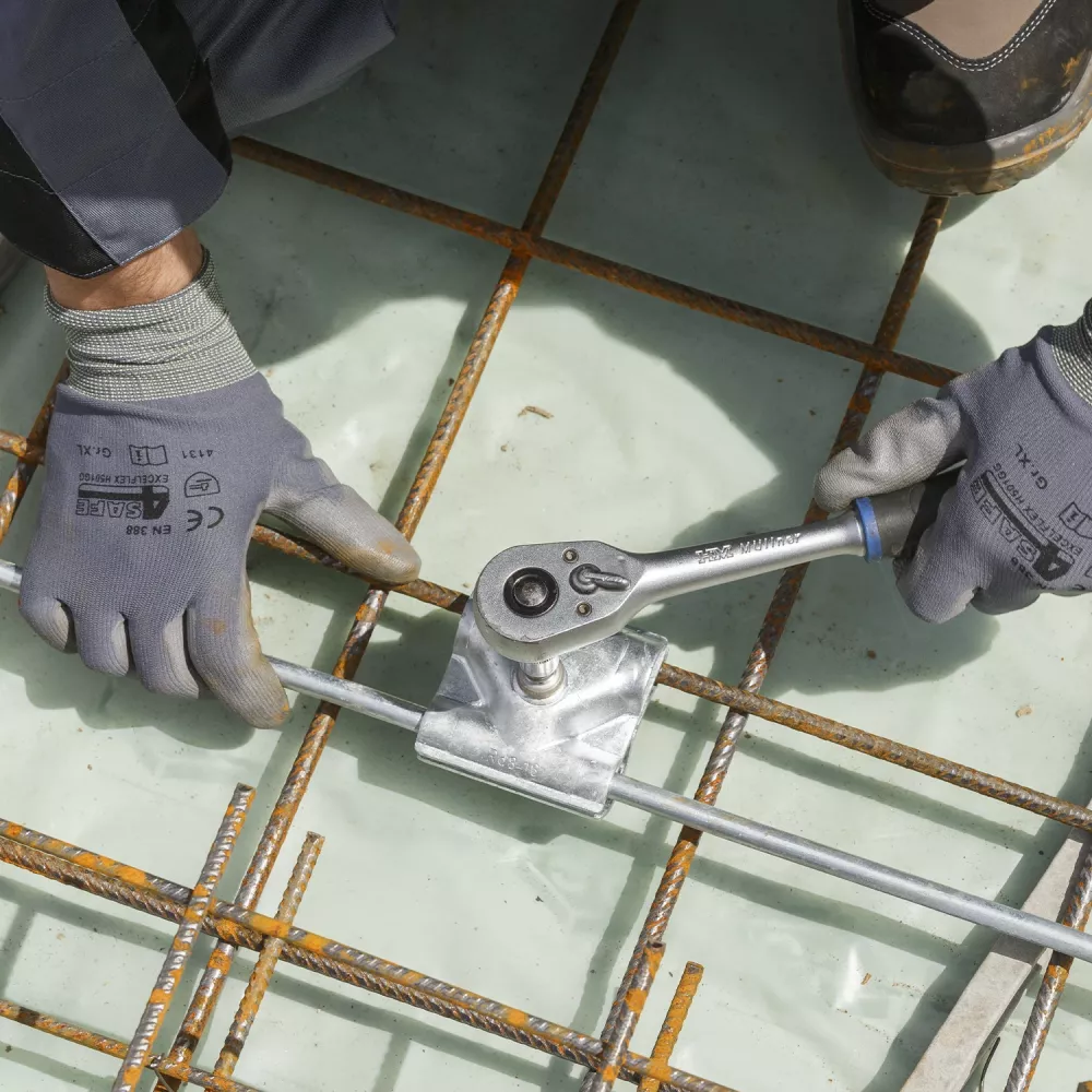 Worker tightening shear-head screw on foundation earthing clamp with ratchet for lightning protection grounding system