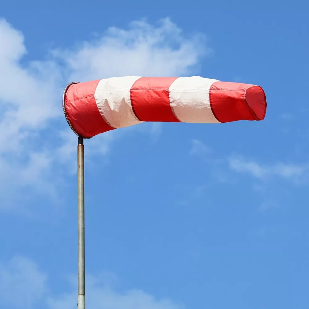 Red and white windsock on a pole against a blue sky with clouds.