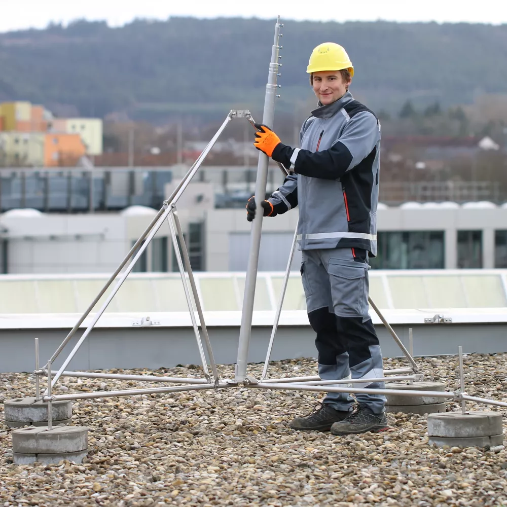 Technician installing lightning protection rod on rooftop using metal support structure and grounding system.