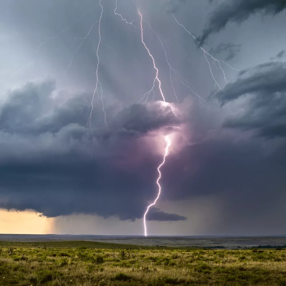 Lightning strike from dark thundercloud to ground over open landscape during storm, bright bolt illuminating sky and horizon.