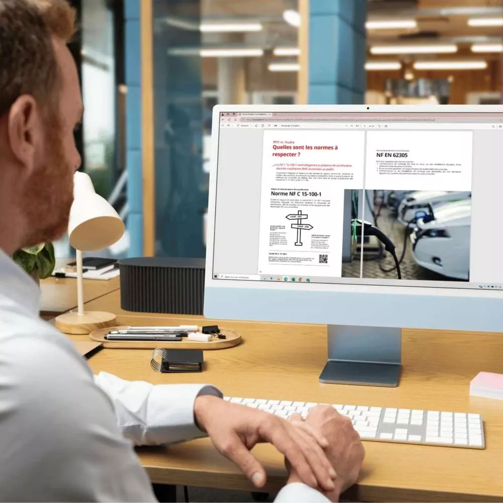Man reading technical guide about electrical standards and surge protection on desktop monitor in modern office workspace.