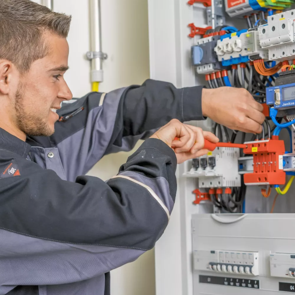 Electrician installing surge protection device in electrical panel with wiring, circuit breakers and measurement equipment.