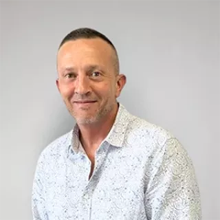 Portrait of a man with short hair, wearing a light patterned shirt.