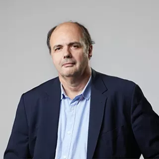 A studio portrait of a man wearing a dark blazer over a light blue shirt.
