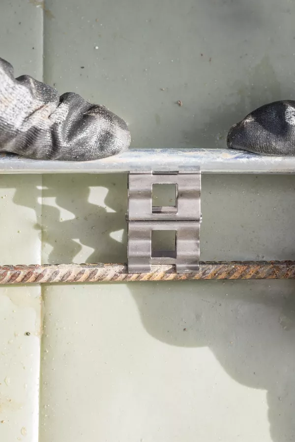 Gloved hands pressing a metal clip between two parallel steel rods against a light-colored surface.
