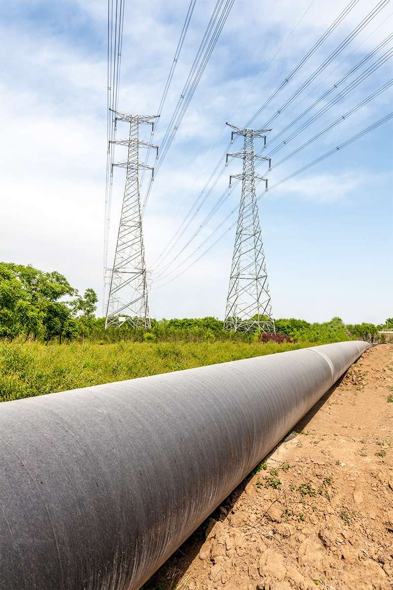 Ligne à haute tension et pipeline dans une prairie verte, sur fond de forêt.