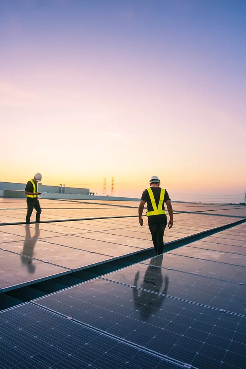 Two people on a flat rooftop with photovoltaic system. Sunset in the background.