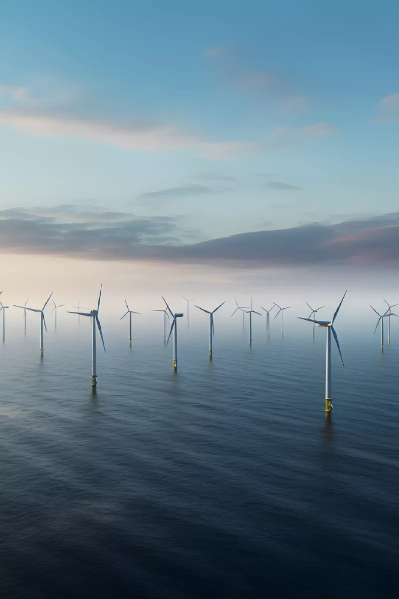 Group of offshore wind turbines standing in calm sea under a partly cloudy sky.