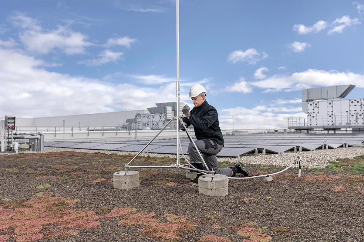 Man wearing a safety helmet installs a lightning rod on a green roof with a solar power system.