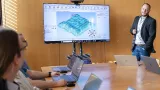 Training room with participants using laptops while a presenter explains a 3D electrical planning model on a large display.